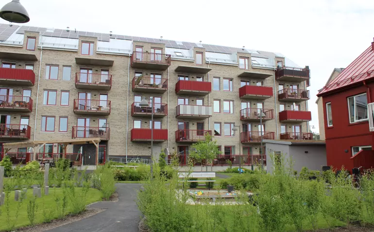 Grå tegelfasad på ett flerbostadshus med balkonger i rött 